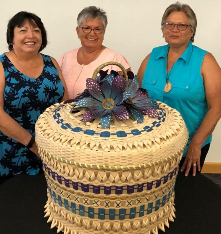 Akwesasne basketmakers (left to right) Nanci Ransom, Sheila Ransom, and Debbie Cook-Jacobs display a basket collaboratively made by the entire Akwesasne community.
